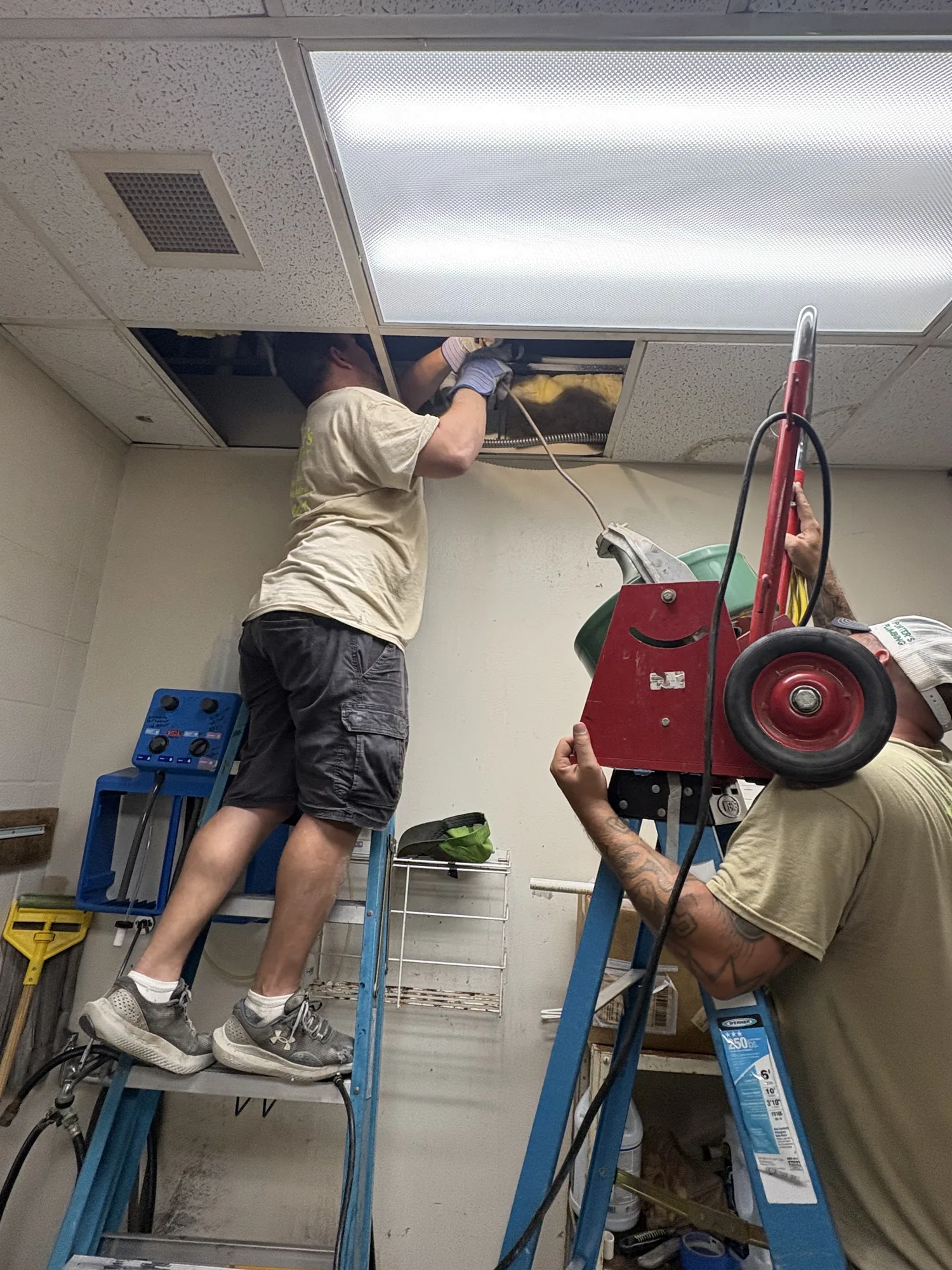 Crew clearing a clogged AC condensate drain line through the ceiling at Wesley Praise Center in Beaumont, TX